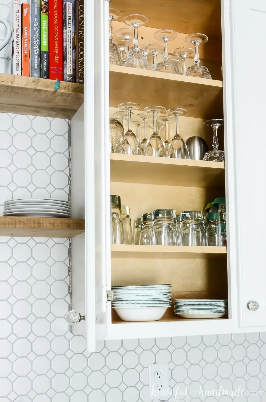 White 42" upper cabinet with goblets, wine glasses, cups and bowls inside with one door open showing the concealed hinges on the inside of the cabinet door. 