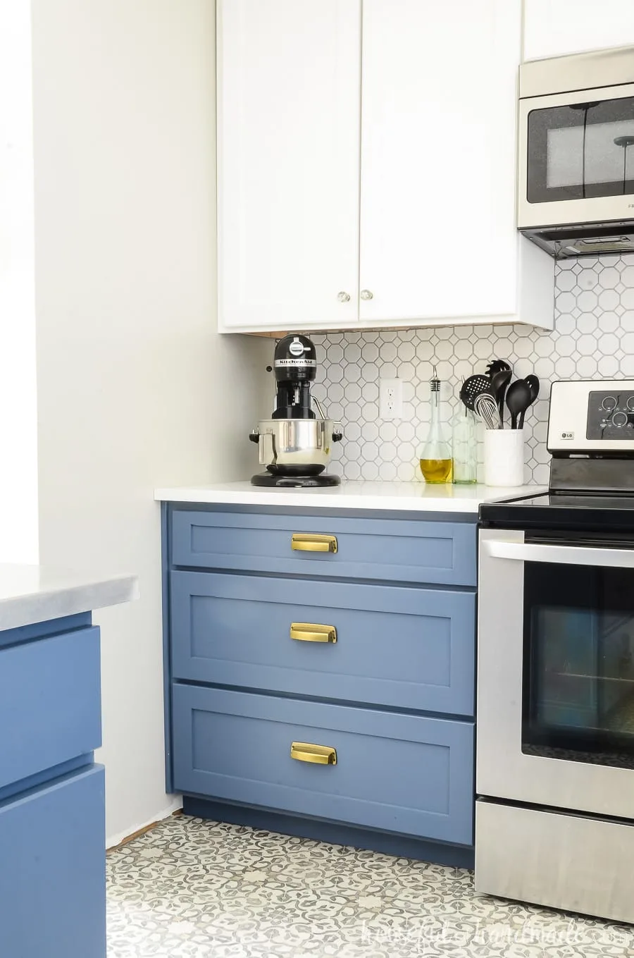 Blue painted drawer base cabinet with 3 drawers next to the stove with white upper cabinets, tile backsplash and countertop.
