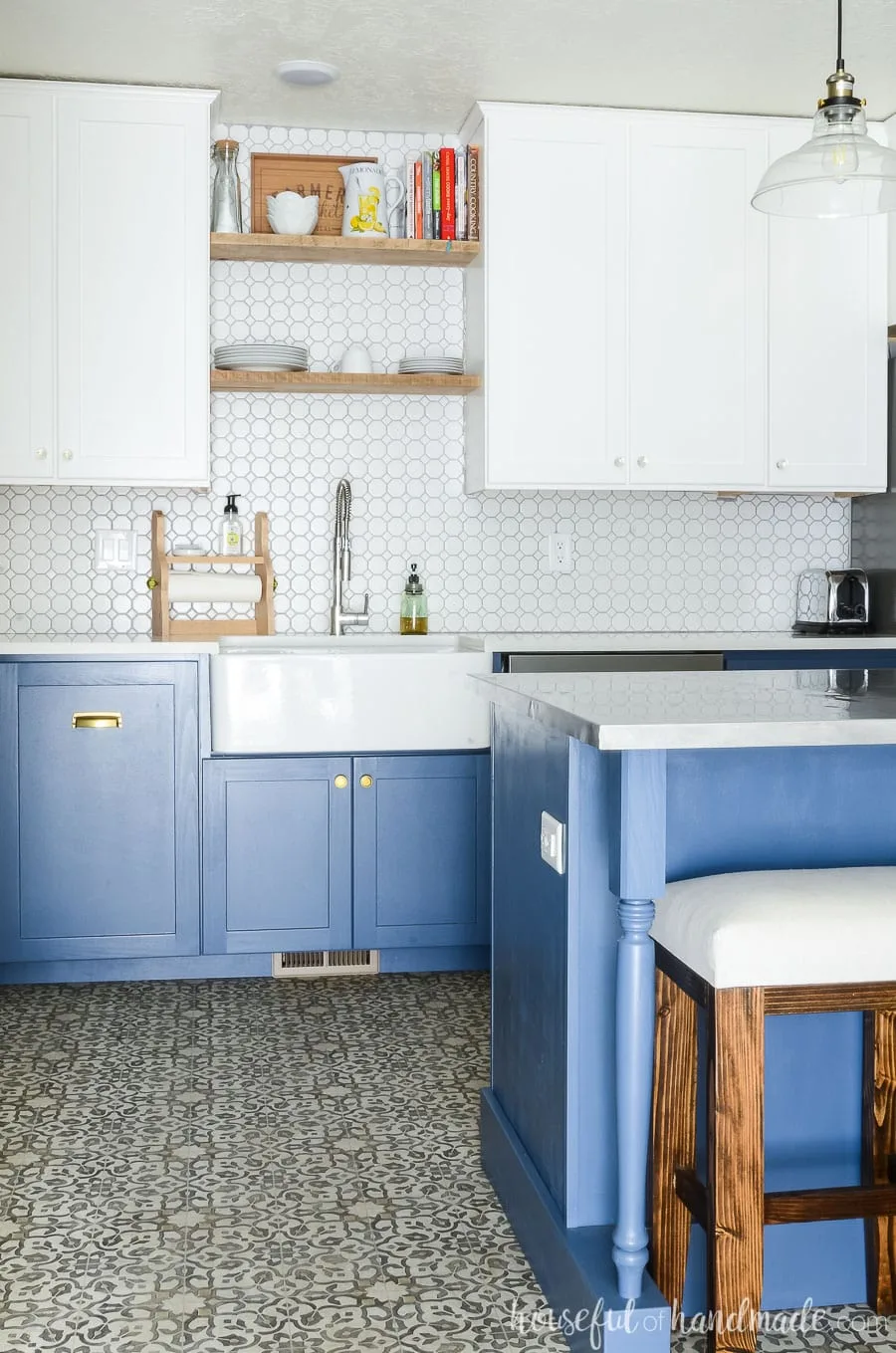 Two tone kitchen with white upper cabinets and blue base cabinets. Apron front kitchen sink with rustic open shelving. Patterned vinyl flooring.