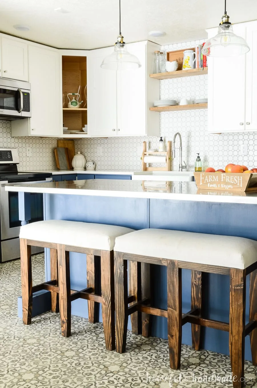 Blue farmhouse kitchen island with bar stool benches at it. White two tone kitchen cabinets in the background.