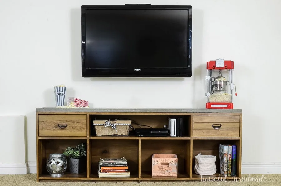 Rustic TV stand with concrete top against a white wall with TV mounted above it. 