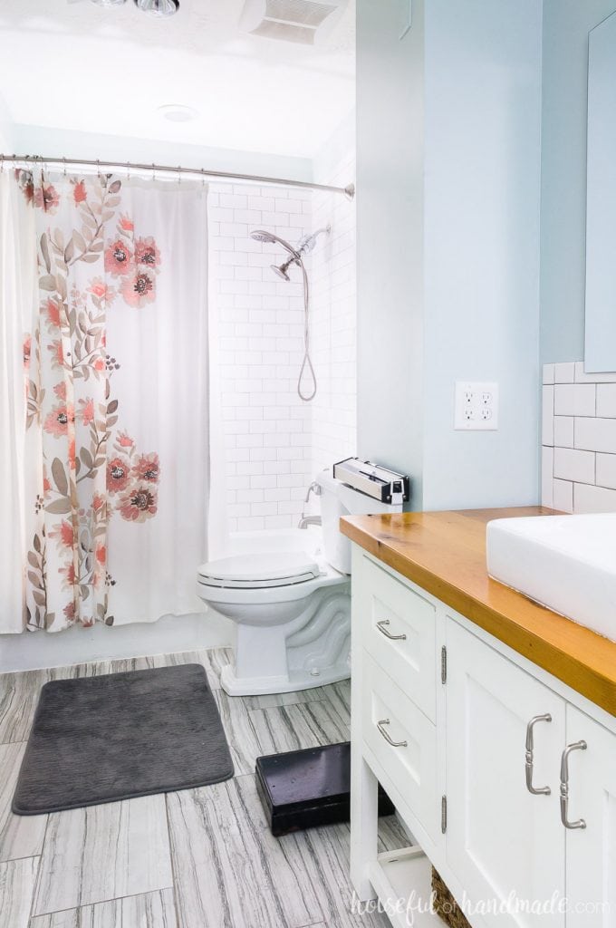 Bathroom with individual subway tiles around the tub surround, with a watercolor floral shower curtain and white vanity with wood top.