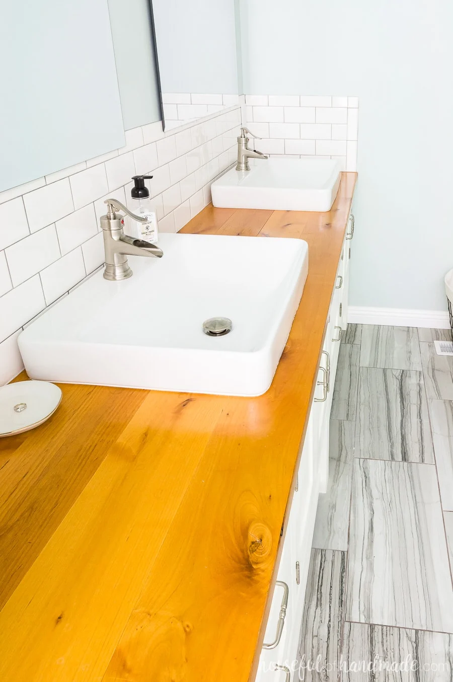 A spa-like master bathroom retreat with alder wood vanity top. Two large vessel sinks sit on top and gray textured porcelain tiles on the floor. 