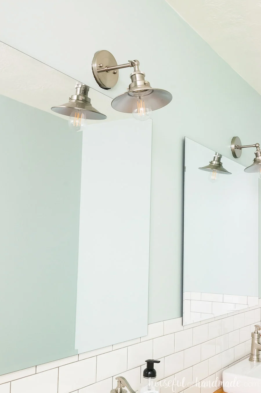 Close up of the frameless beveled mirror and brushed nickel sconces on the farmhouse green walls in the master bathroom retreat. 