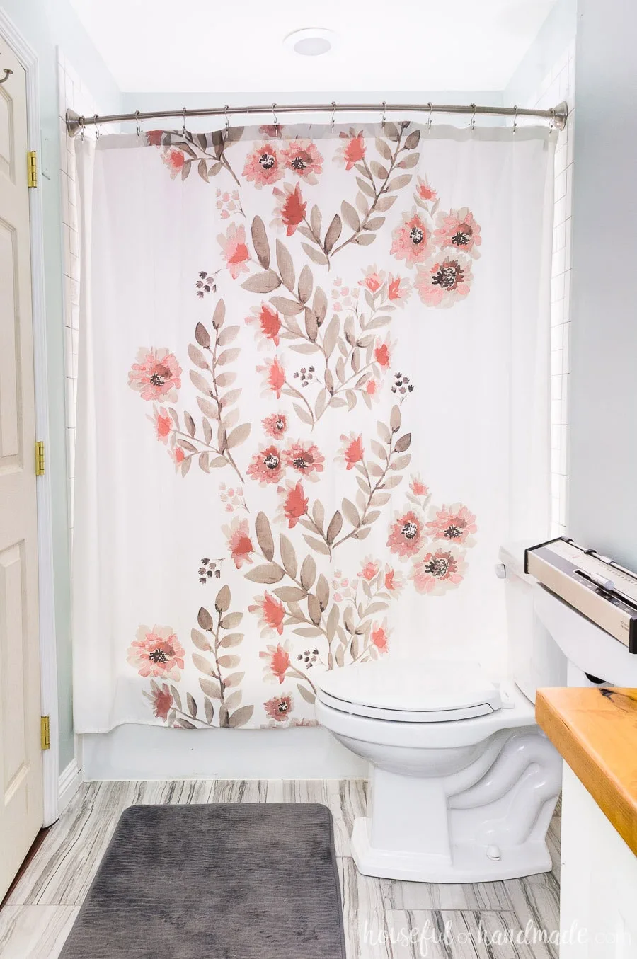 Beautiful master bathroom retreat created with watercolor floral shower curtain, gray porcelain tile, and white vanity with wood vanity top.