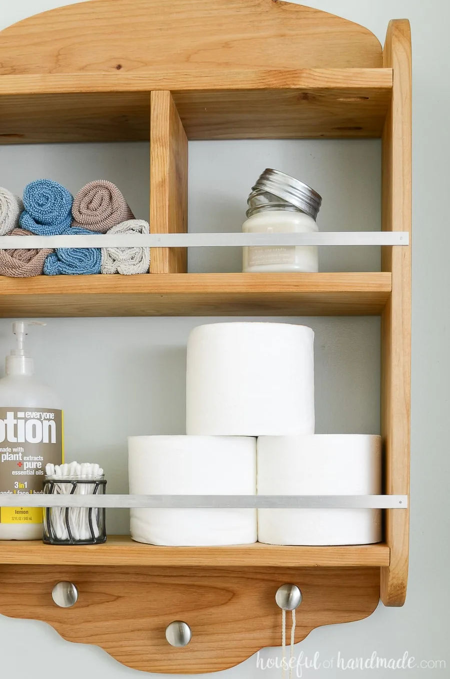 Clos-up view of the bathroom storage shelves. Metal railings keep items on the shelves and knobs below for hanging.