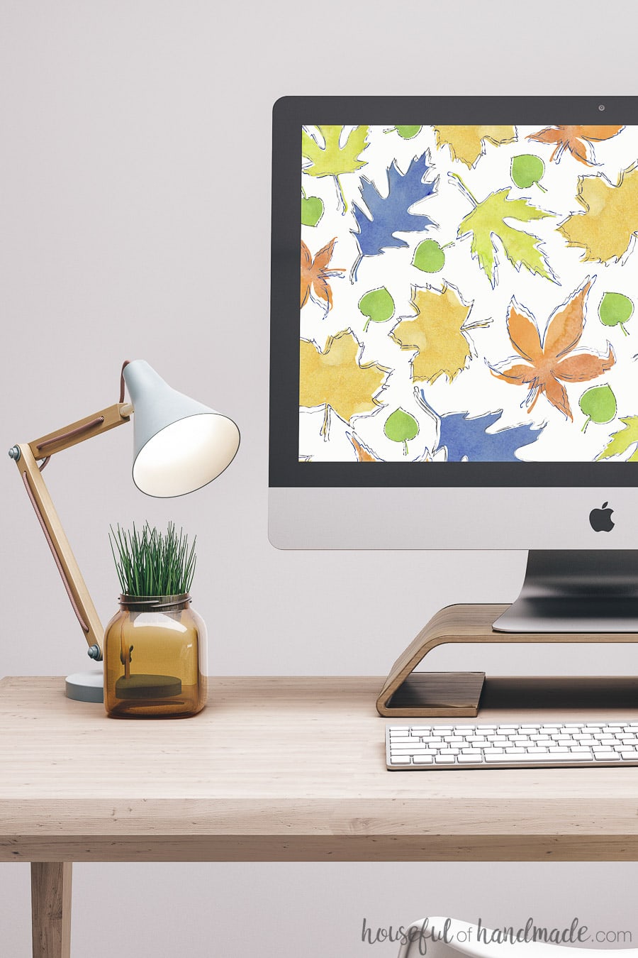 Computer on desk with lamp and plant showing free digital backgrounds on computer. Colorful autumn leaves digital wallpaper. 