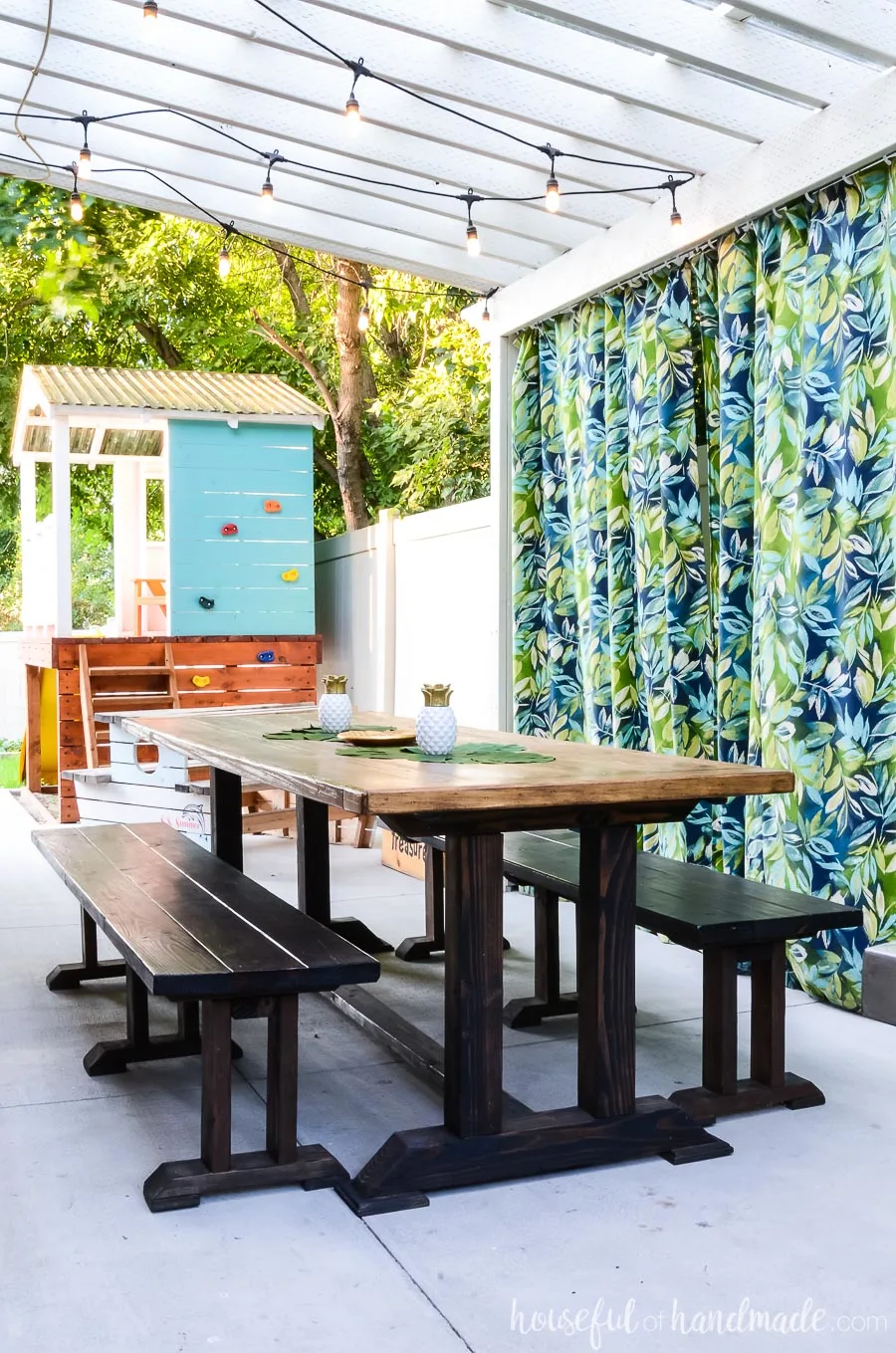 Island inspired outdoor living spaces. Patio pergola with tropical outdoor curtains and a large outdoor dining room. Kids play house in the background.