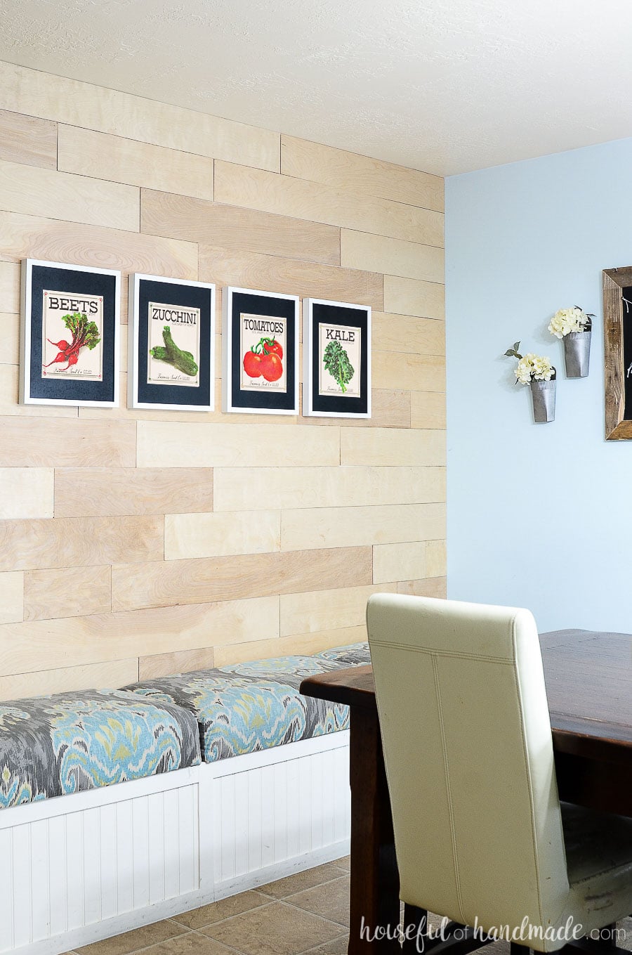 Vegetable seed packet art of beets, zucchini, tomatoes, and kale on the wood accent wall of the dining room. 