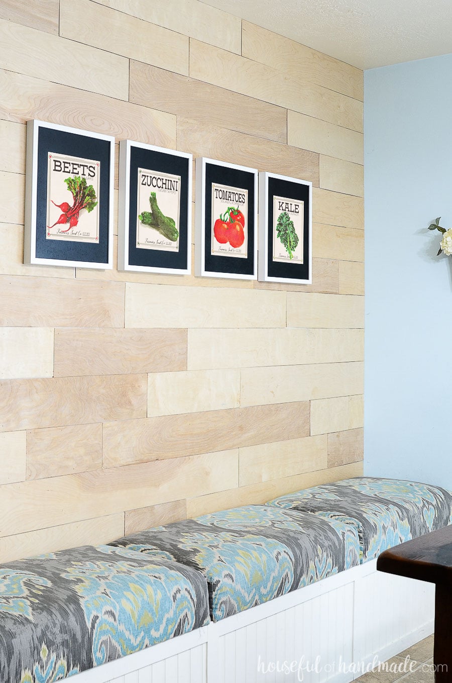 Wood wall with built in dining room bench and 4 vegetable seed packet art prints above it. 