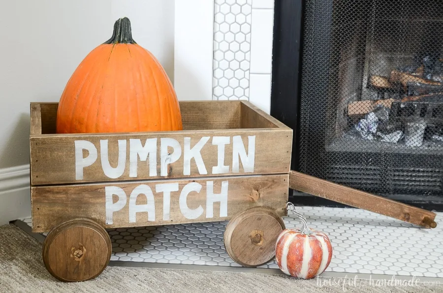 Close up of the decorative wood wagon on the hearth with two pumpkins. 