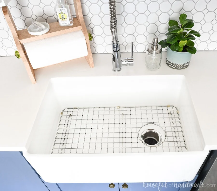 White fireclay farmhouse sink in a kitchen with white countertops and stainless steel sink grid in the bottom. 