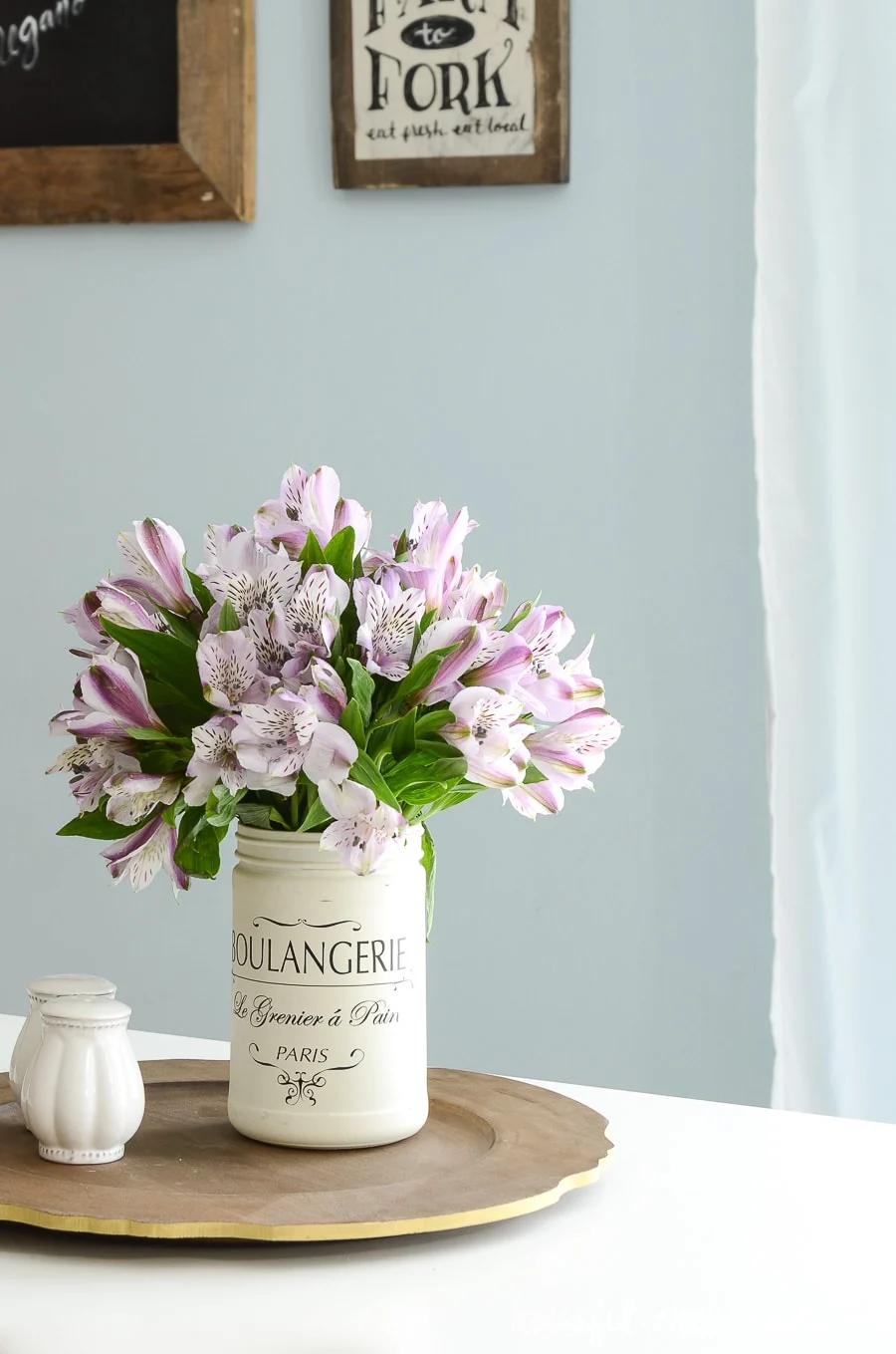 DIY farmhouse kitchen canister used as a vase with purple flowers sitting on an upcycled wood sign into a tray. 
