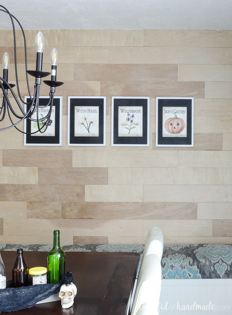 Printable Halloween art in white frames with black mats. Hanging on a wood plank wall in the dining room. 