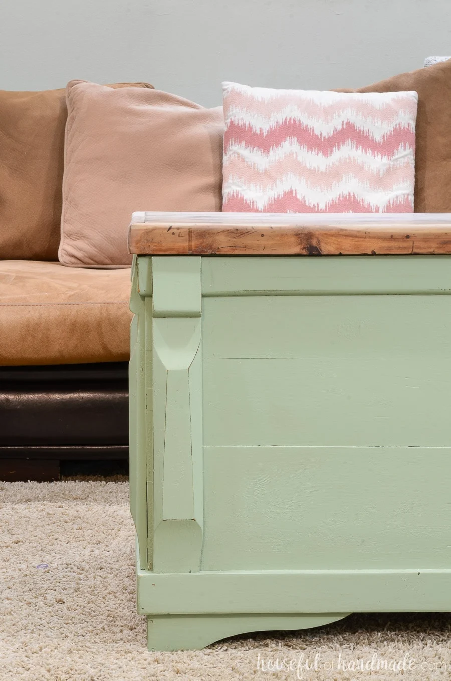 Close up of the refinished blanket chest being used as a coffee table. The base of the chest is painted green with slight distressing and the top is left wood toned. 