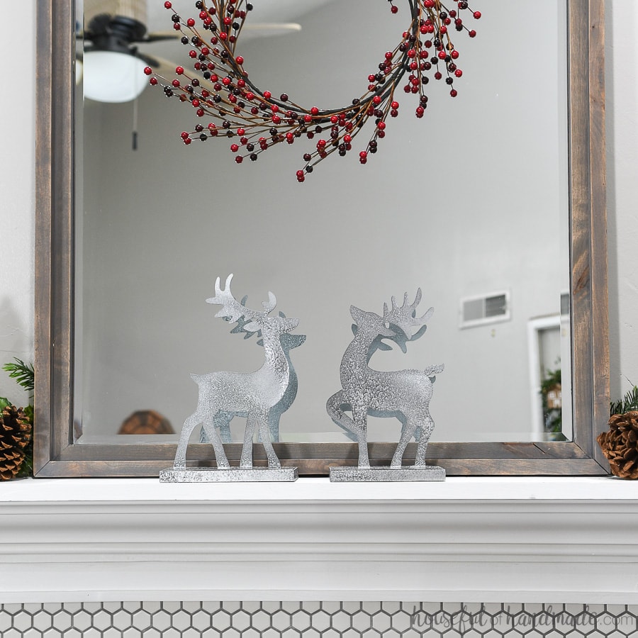 Two Christmas reindeer decorations on the mantel in front of the mirror with classic mantel decor. 