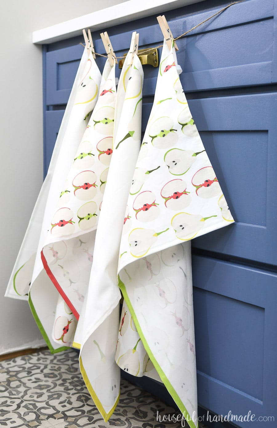 Four decorative fall tea towels hanging over kitchen cabinets. 