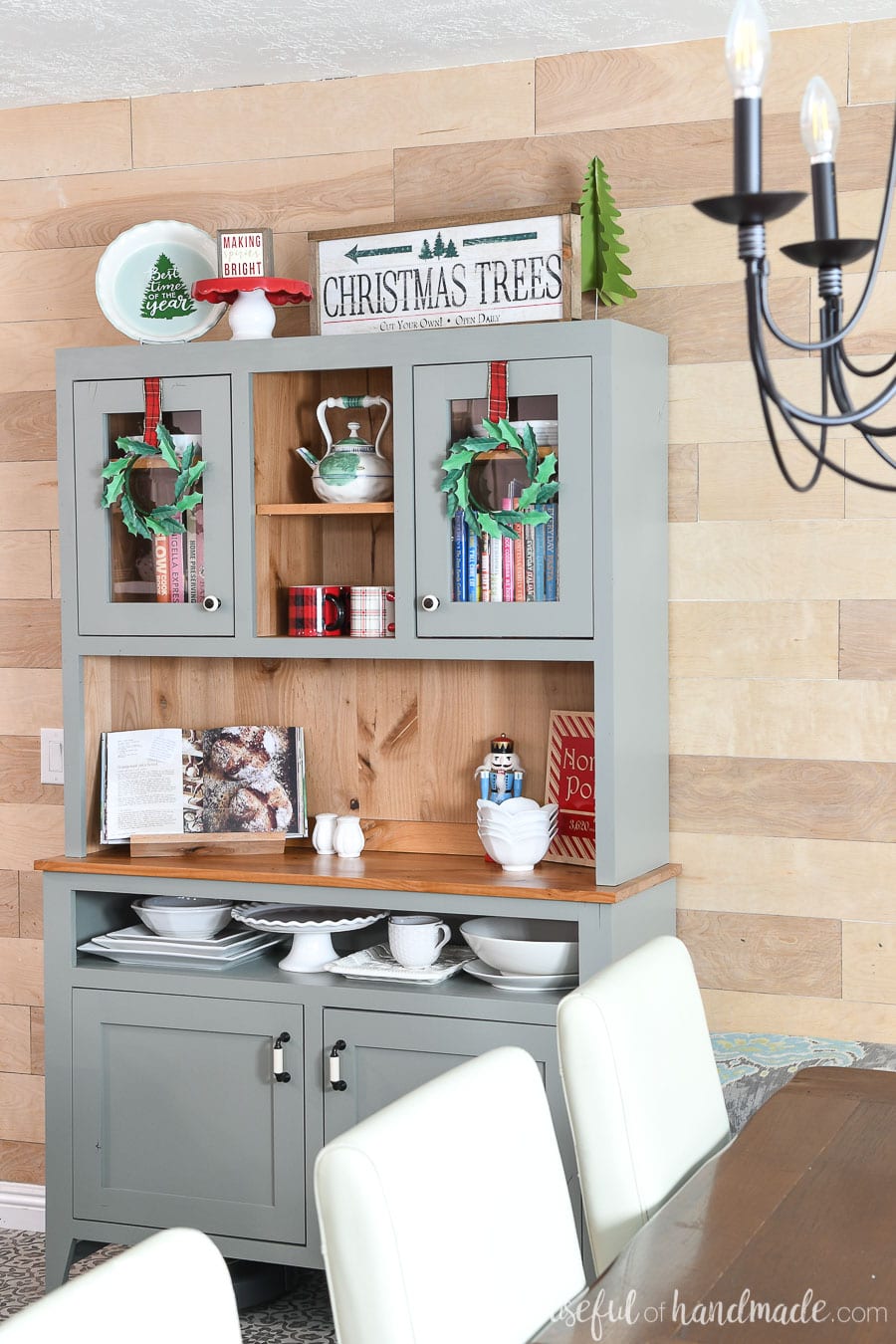 Dining room hutch all decorated for Christmas with paper holly wreaths hanging on the cabinet doors. 