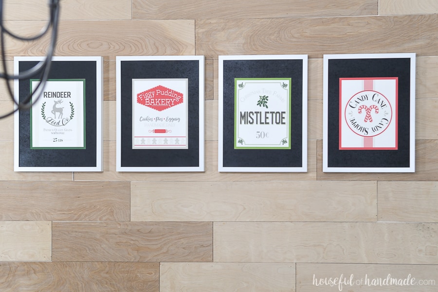 View of the 4 printable Christmas signs in white picture frames with black mats. 