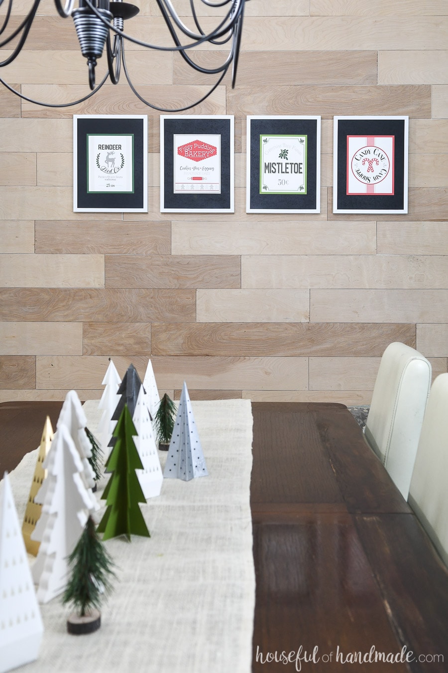 Four printable Christmas signs hanging in white frames on a wood wall. 