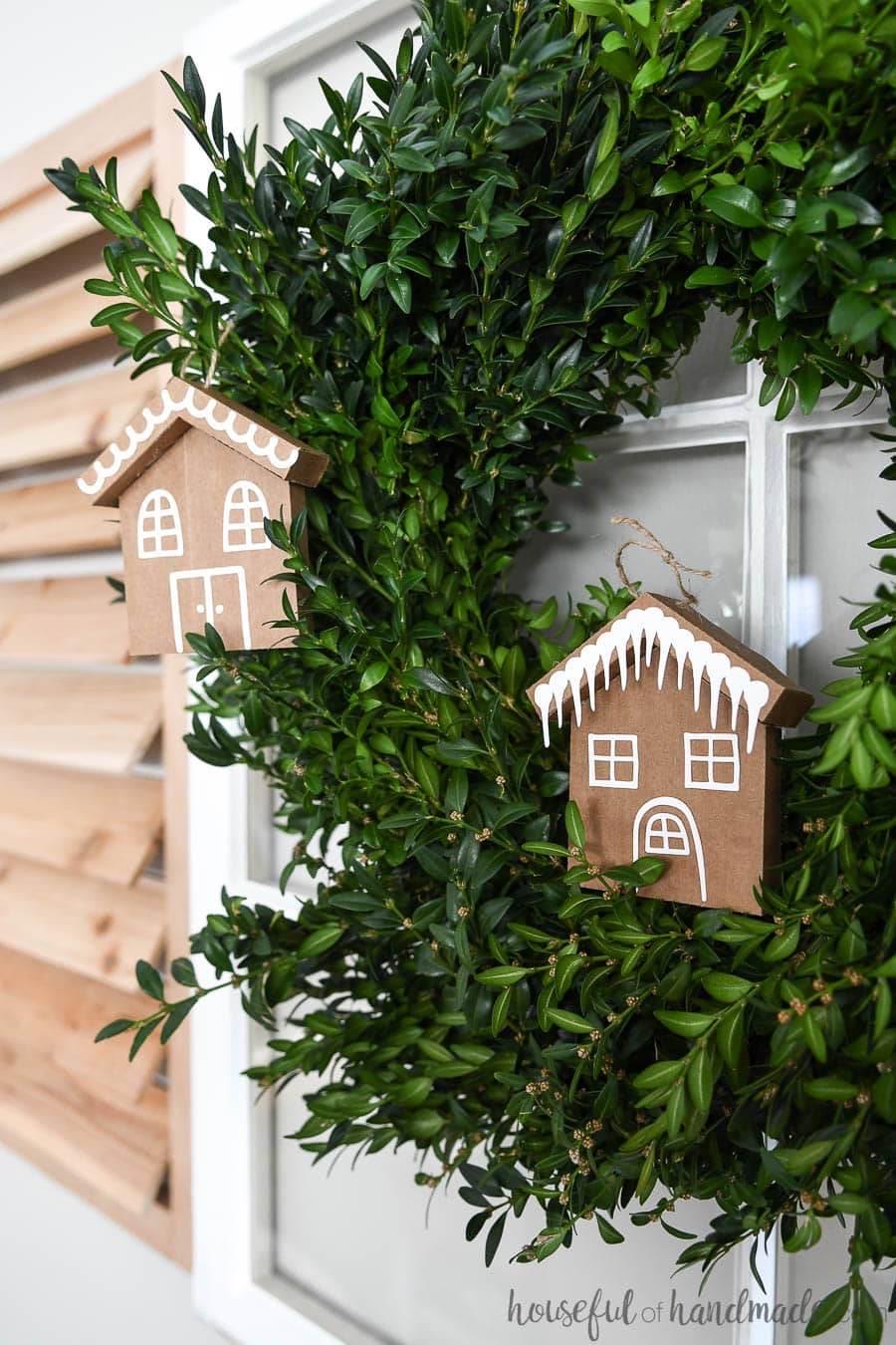 Boxwood wreath with paper Christmas ornaments on it.