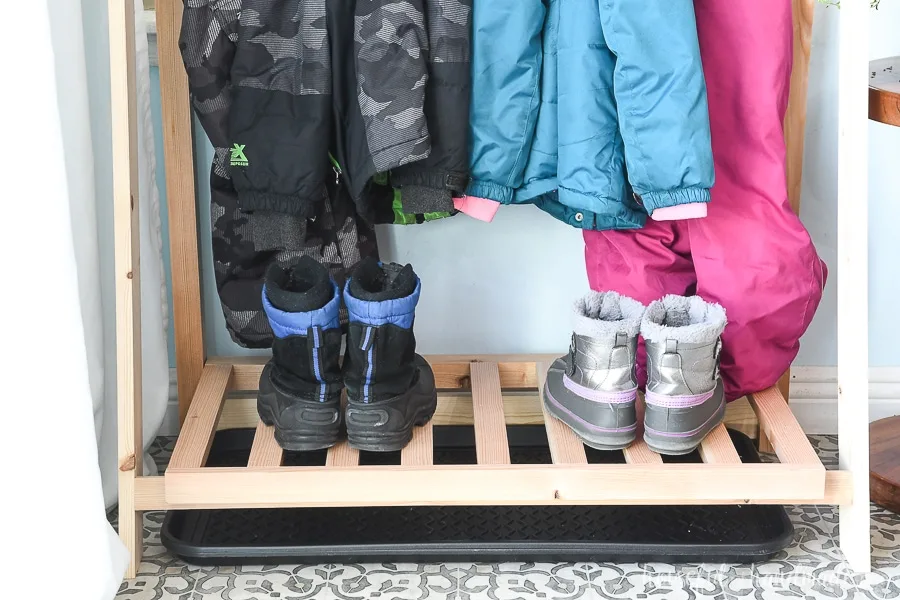 Close up of the bottom shelf of the fold-up storage shelves with snow boots on it and a drip tray below to catch melting snow. 
