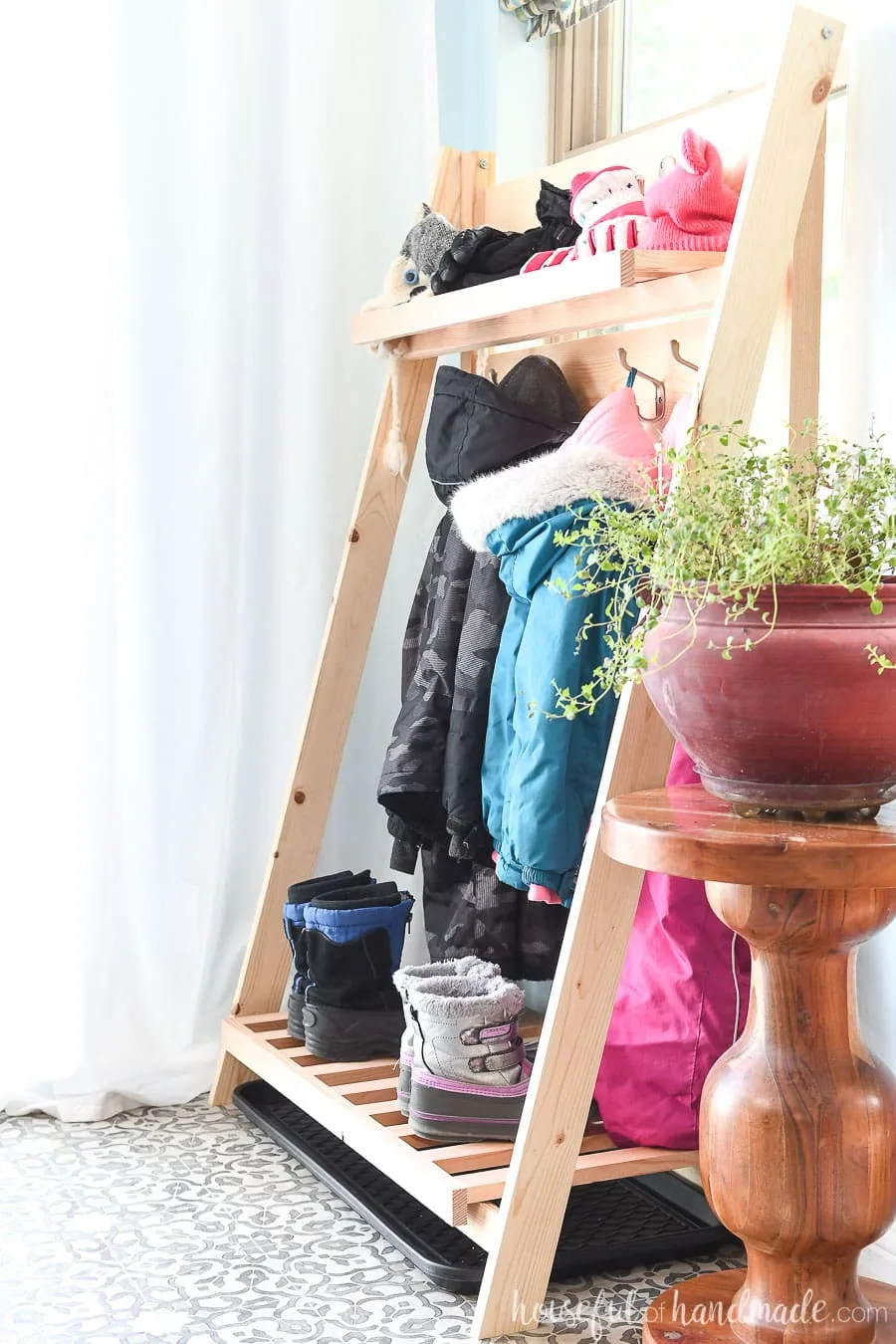 Side view of the collapsible storage shelves holding kids snow pants, coats, gloves and boots to dry. 