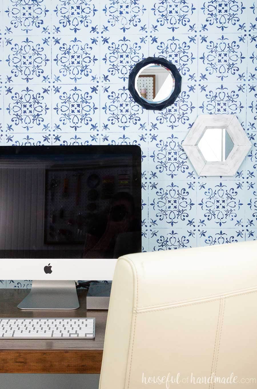 White rustic hexagon wall mirror and navy geometric mirror on a wall behind a computer. 