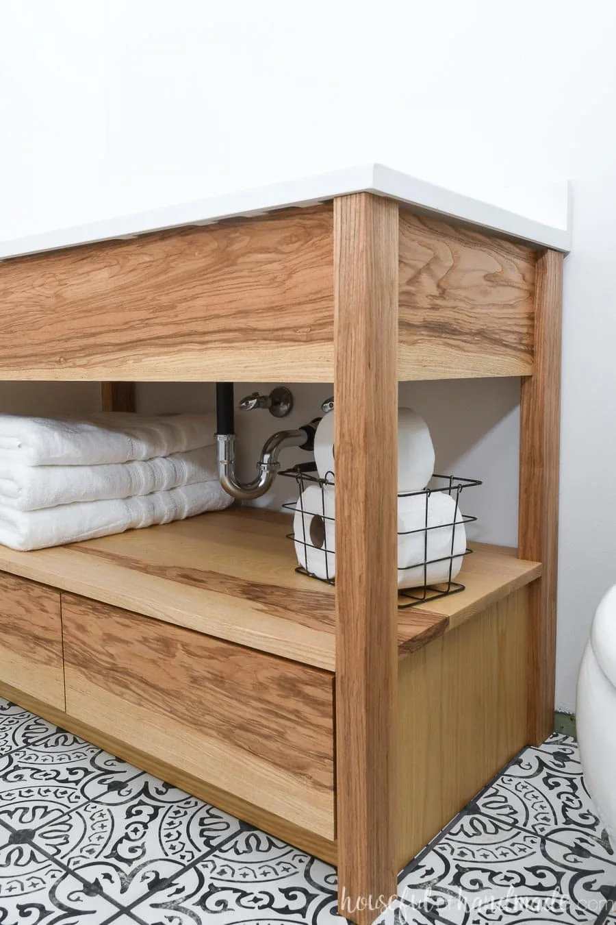 Closeup of the open shelf on the DIY bathroom vanity with towels and toilet paper stored on it. 