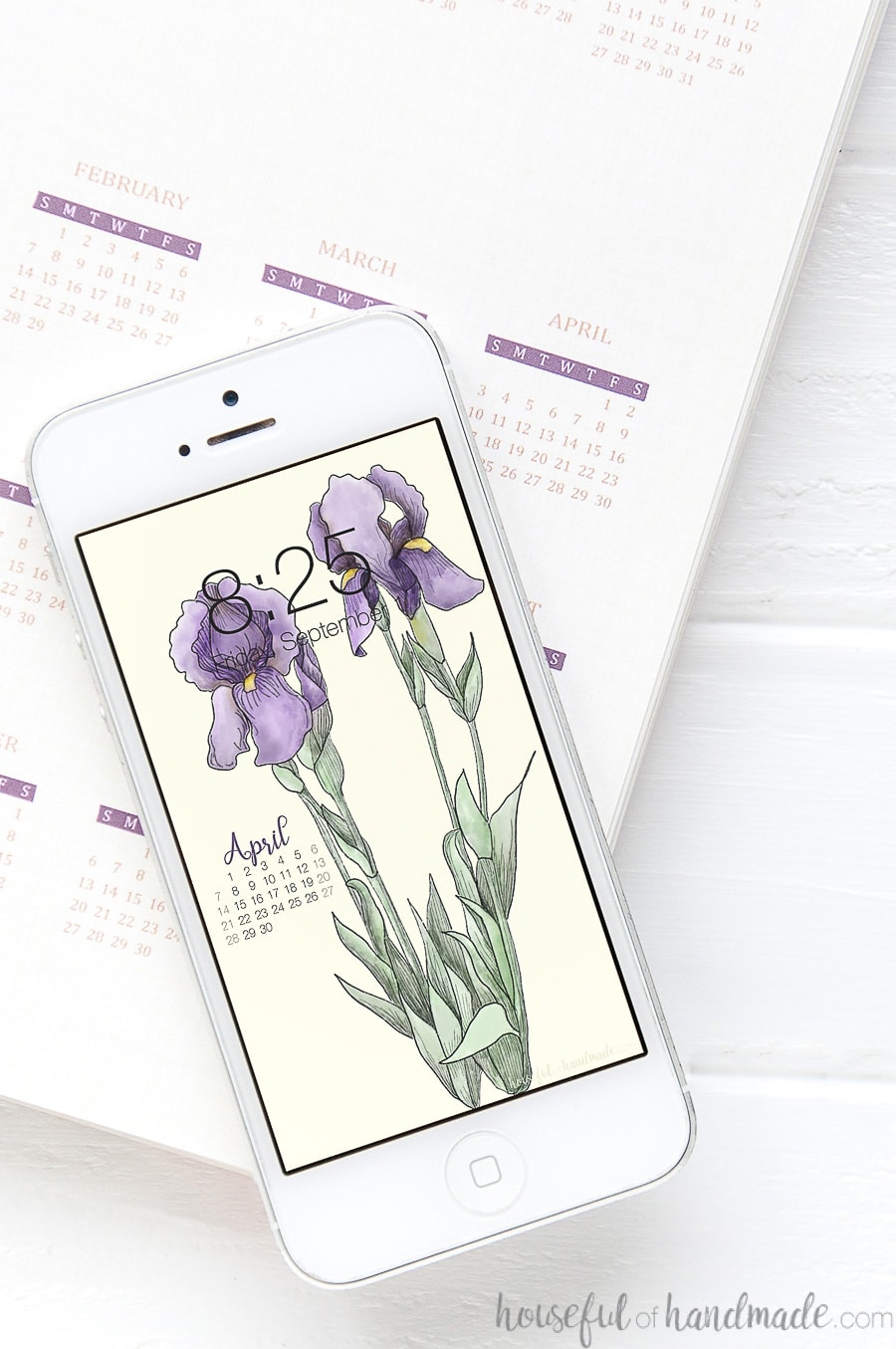White iPhone with iris wallpaper on the background on top of a planner.