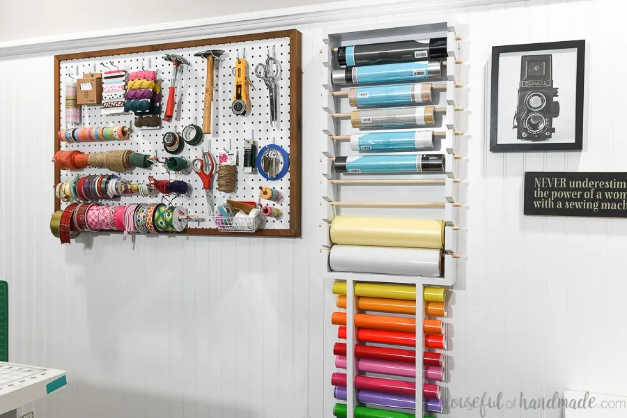 Craft room wall with pegboard storage and vinyl roll storage hanging on it.
