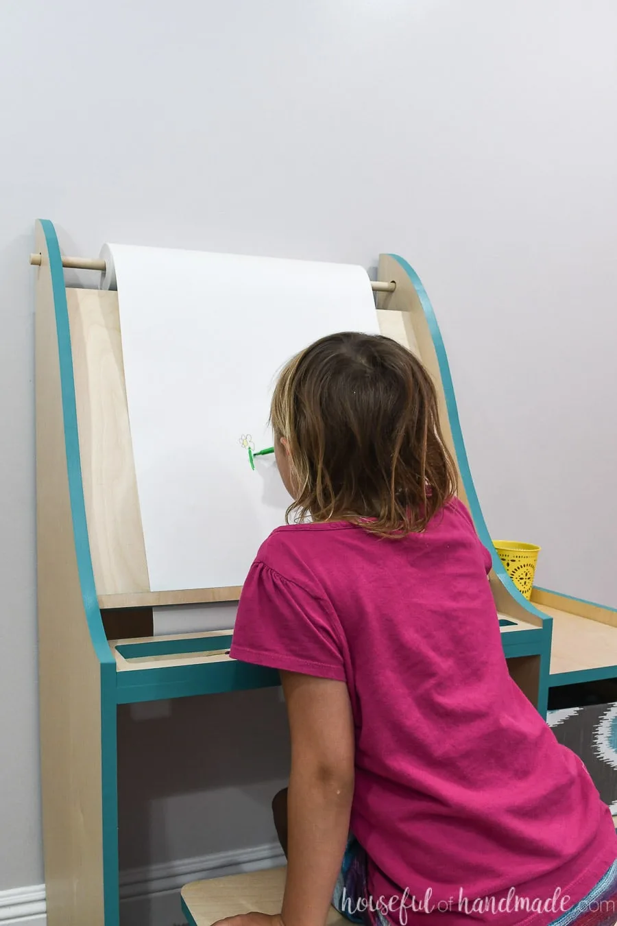 Little girl in pink shirt painting on the DIY art easel using the roll of paper. 