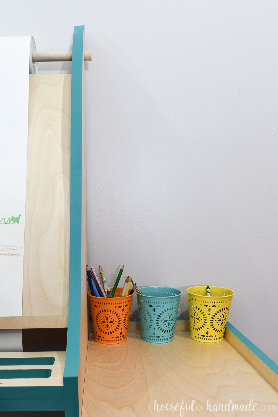 Close up view of the side of the kids art easel with colorful jars holding pencils, paint brushes and crayons. 