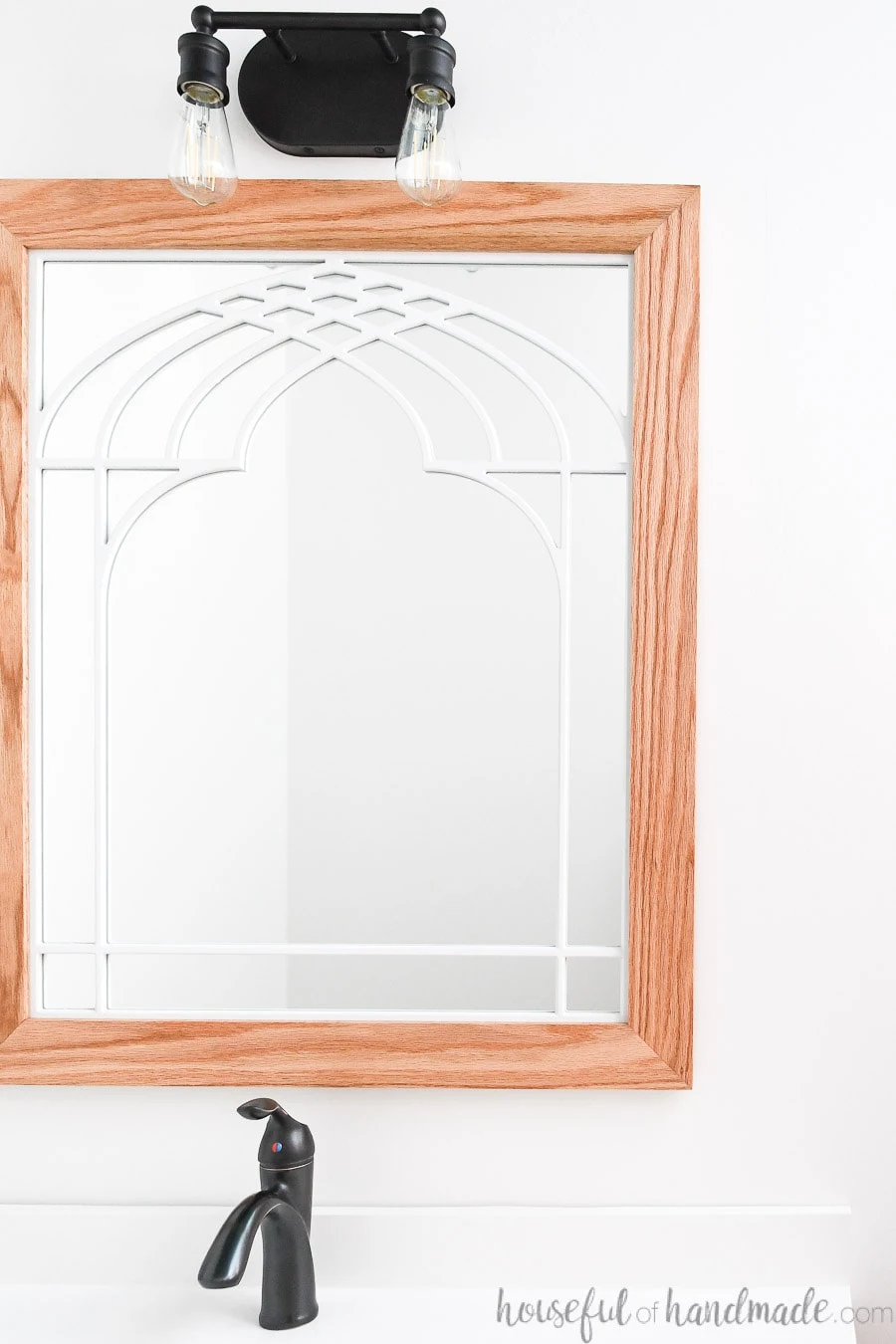 Bathroom mirror that looks like a window with cathedral arch in the center and wood frame. 