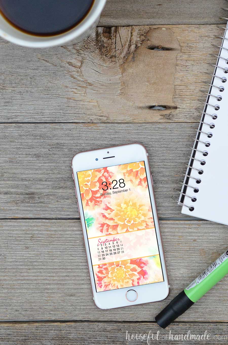 Desk with notepad, coffee, and smartphone with floral wallpaper with September calendar on the screen.