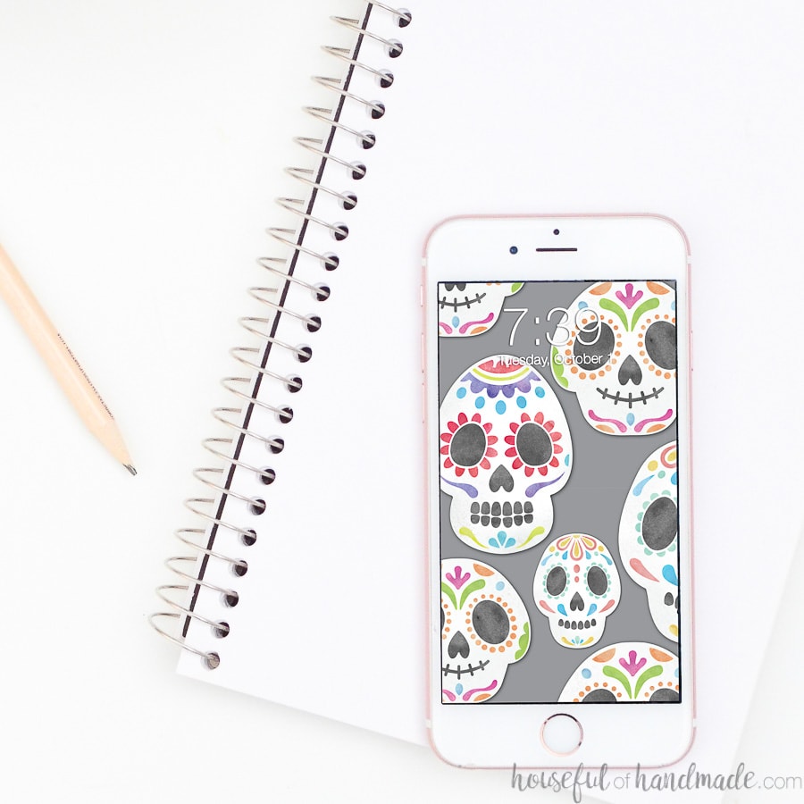 Smartphone with sugar skulls on a gray digital background sitting on a notebook.