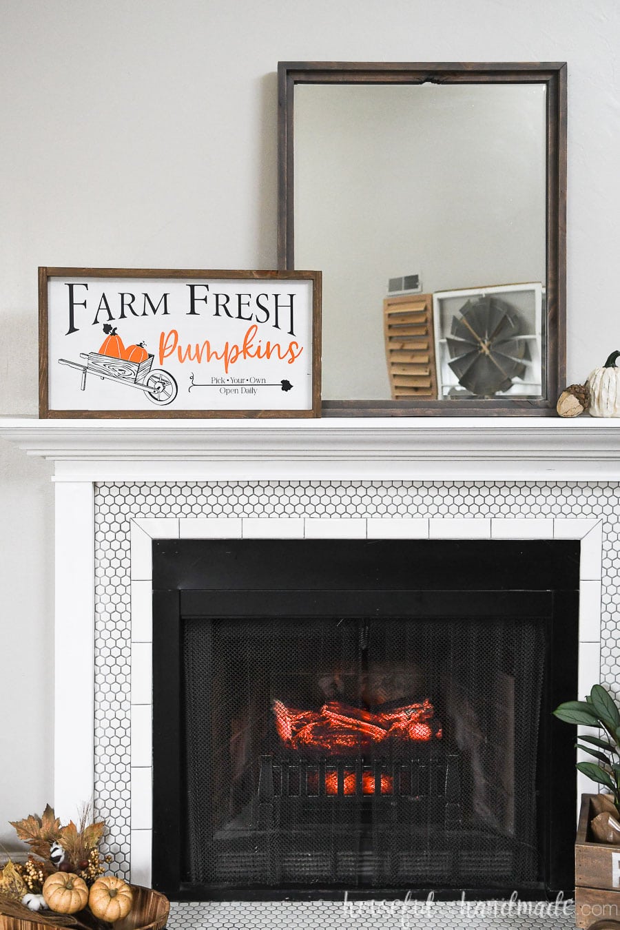 Mantel with fall decoration on it: a wood pumpkin patch sign, pumpkin, acorn, mirror, and fall leaves.