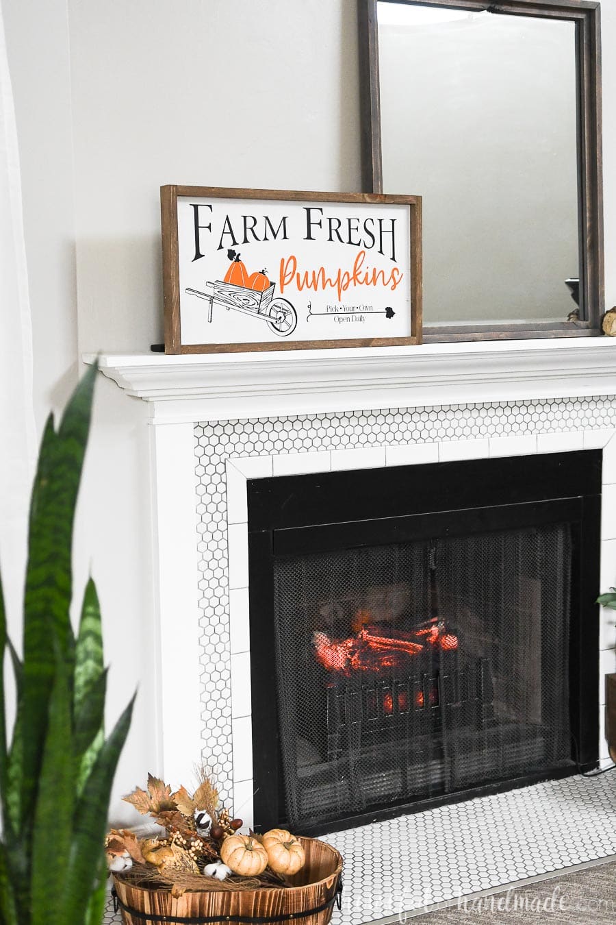 Angled view of a mantel decorated for fall with a fall wood sign and snake plant in the foreground. 