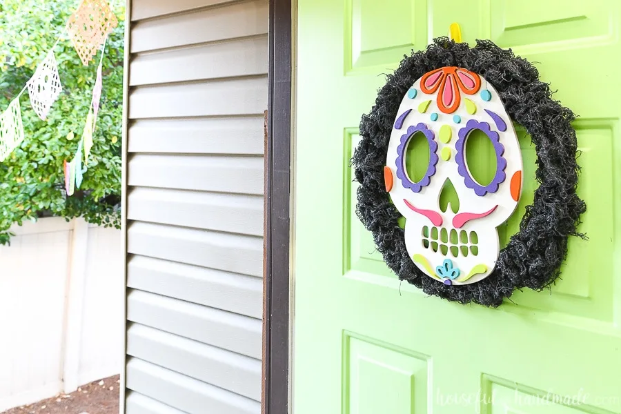 Horizontal view of the green front door open with a sugar skull wreath hanging on it. 