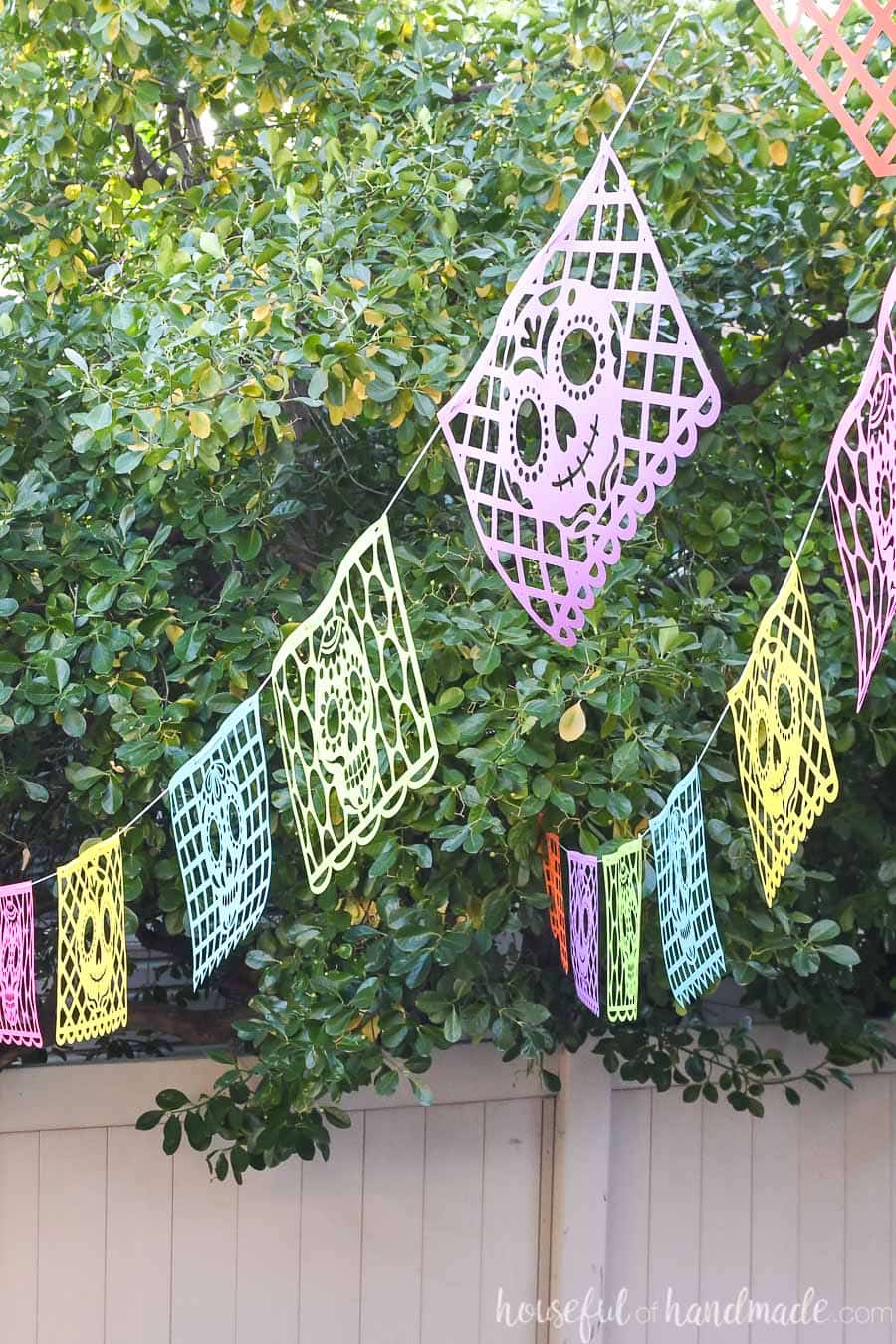 Picture of colorful halloween paper banners hanging outside with sugar skull designs on them. 