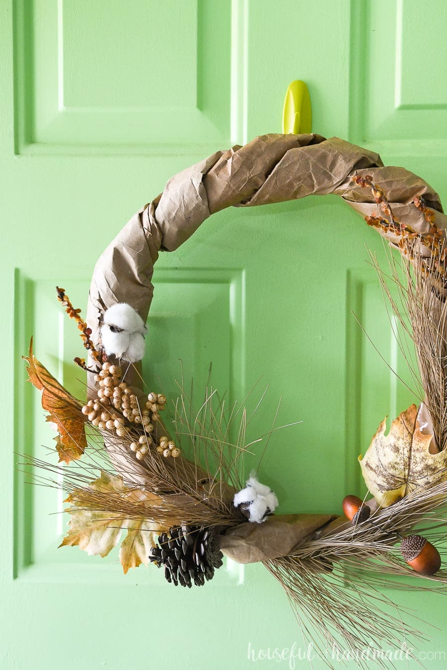 View of the left side of the neutral fall wreath made from a brown paper bag hanging on a green front door. 