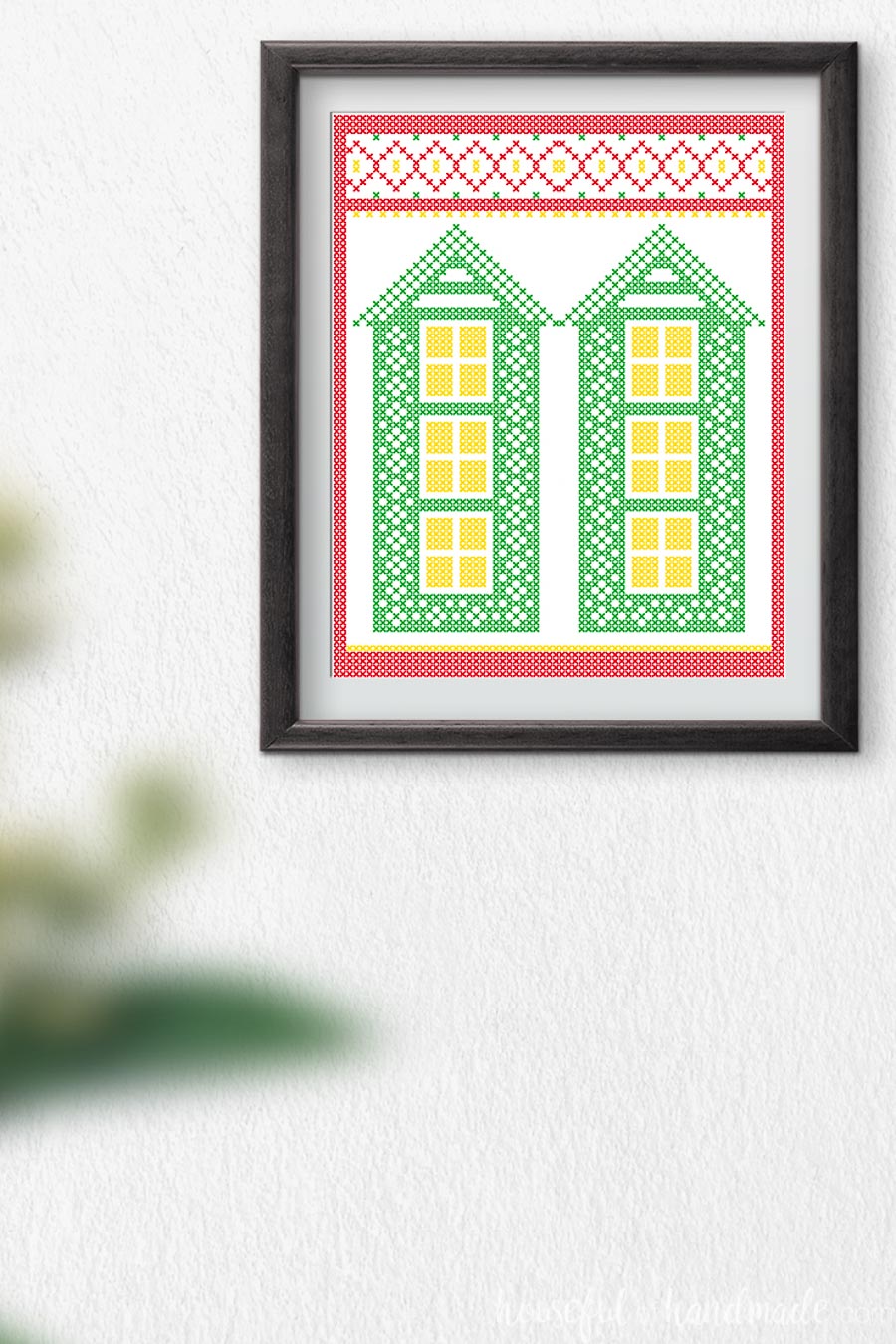 Cross-stitched printable art with two tall green houses and a Christmas border. 