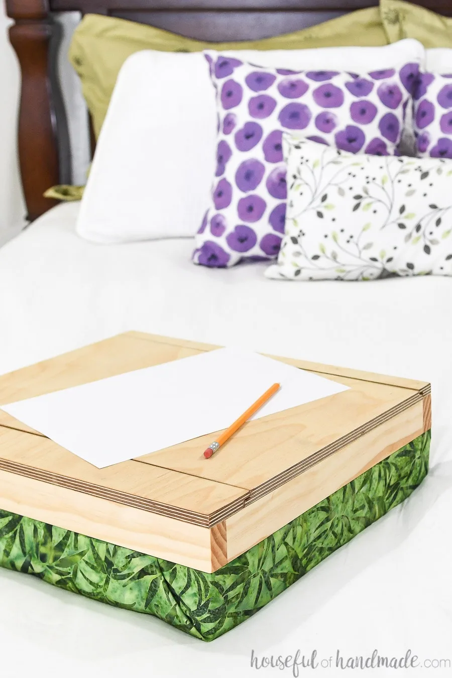 DIY lap desk with cushion covered in green leaf print on a bed. 