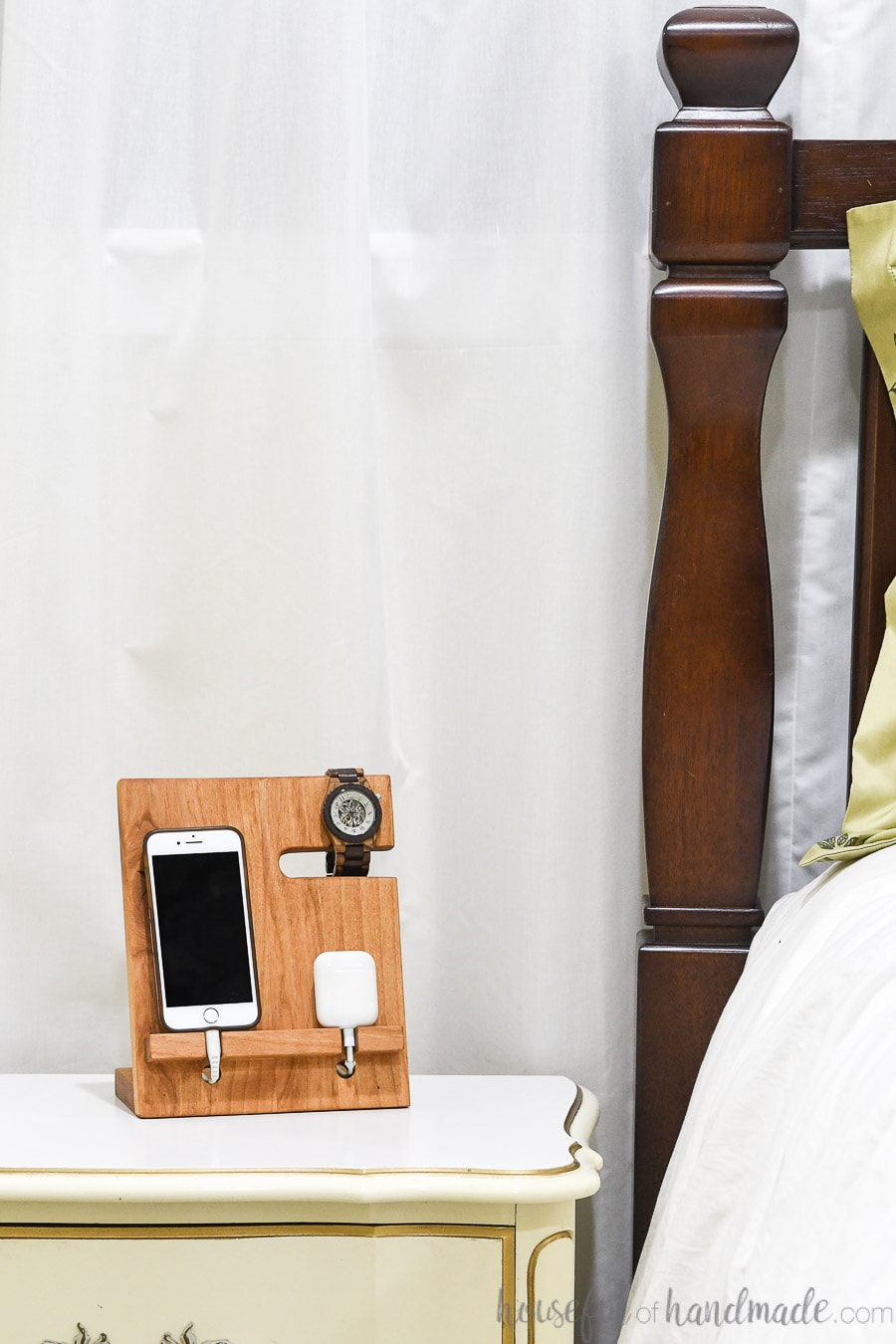 Bedside table organized with all the electronics charging on a wood valet. 