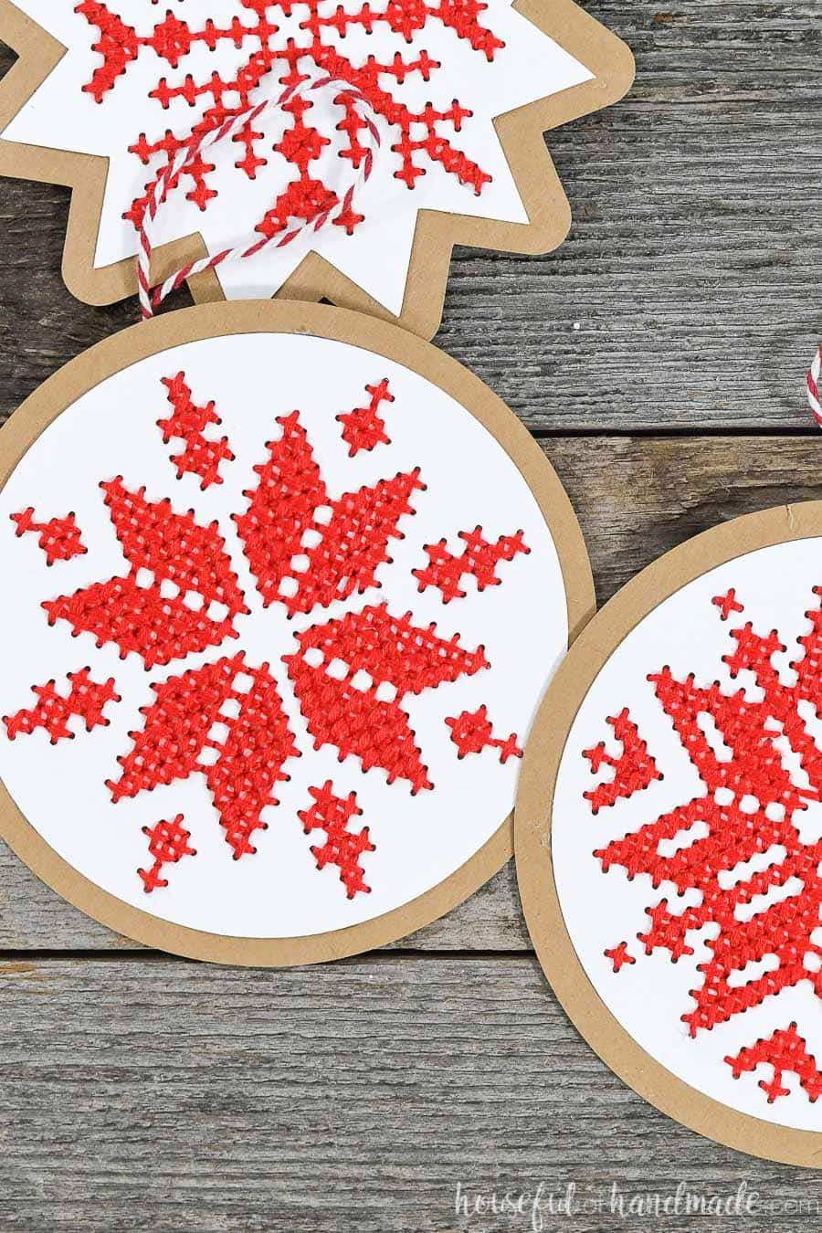 Cross-stitched snowflake designs on paper Christmas ornaments laying on a wood background.