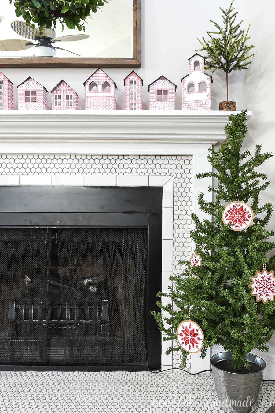 Small Christmas tree in front of a fireplace with red & white Nordic cross-stitched ornaments on it.