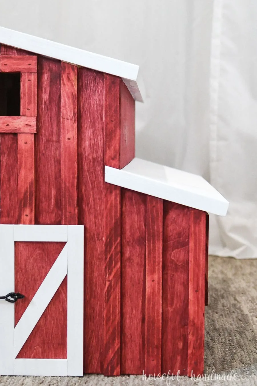 Front view of 1/2 of the wooden toy barn with red stain and white trim. 