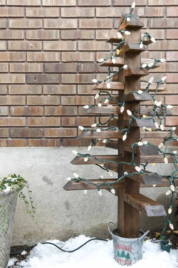 Outdoor Christmas tree made from 2x4s with a bucket for a base with a Christmas tree farm design on it.