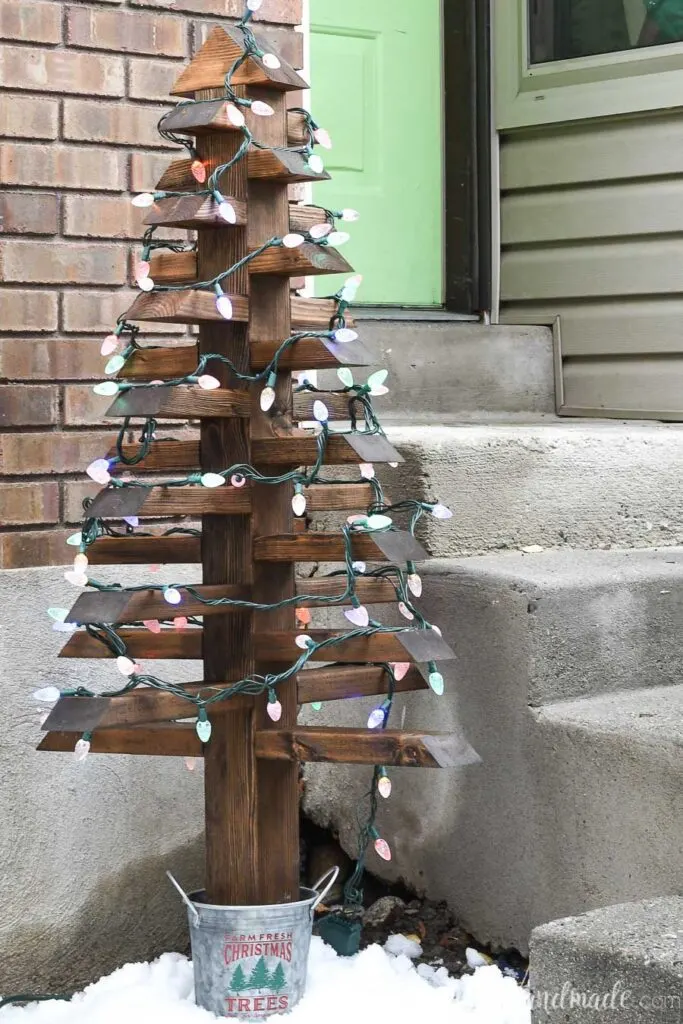 Wood Christmas tree made from 2x4s with a decorative bucket base and lights on it. 