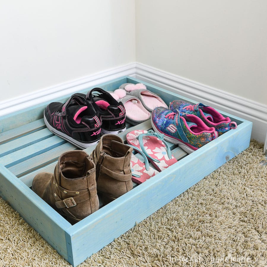 Turquoise stained shoe storage tray in the bottom of a kids closet.